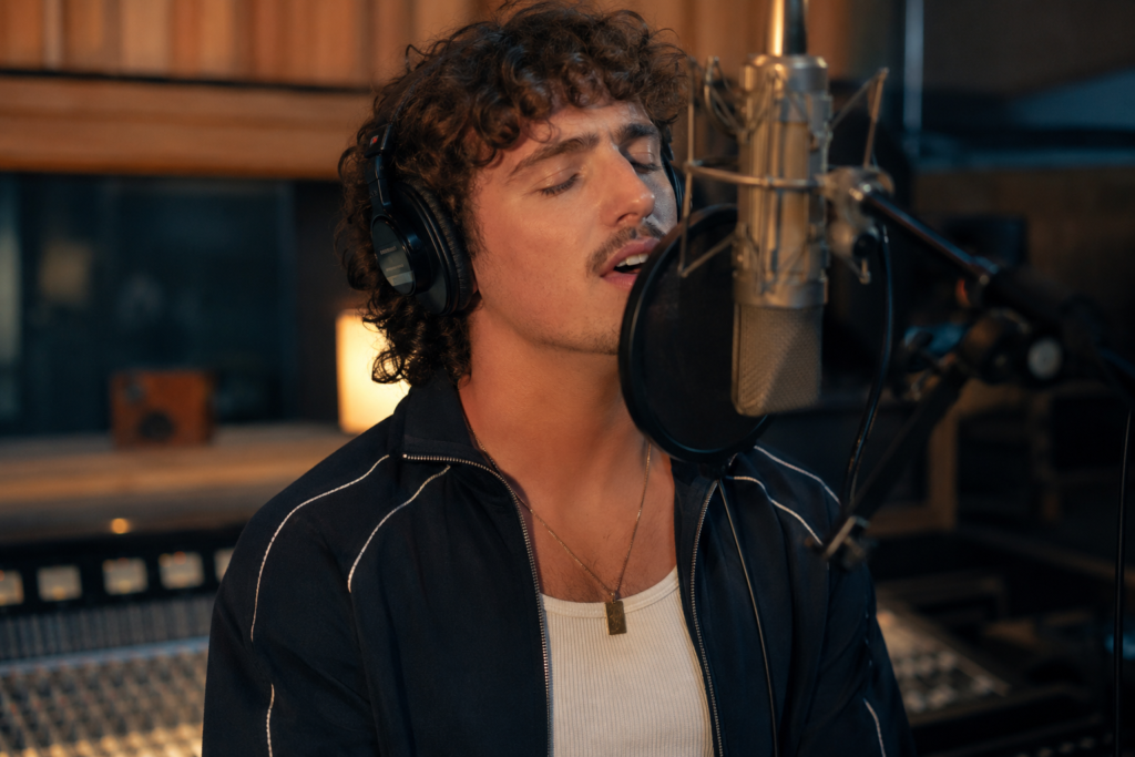 Benson Boone age in a professional recording studio wearing headphones, singing into a microphone, music production equipment visible, realistic studio environment, cinematic lighting, high-resolution photography